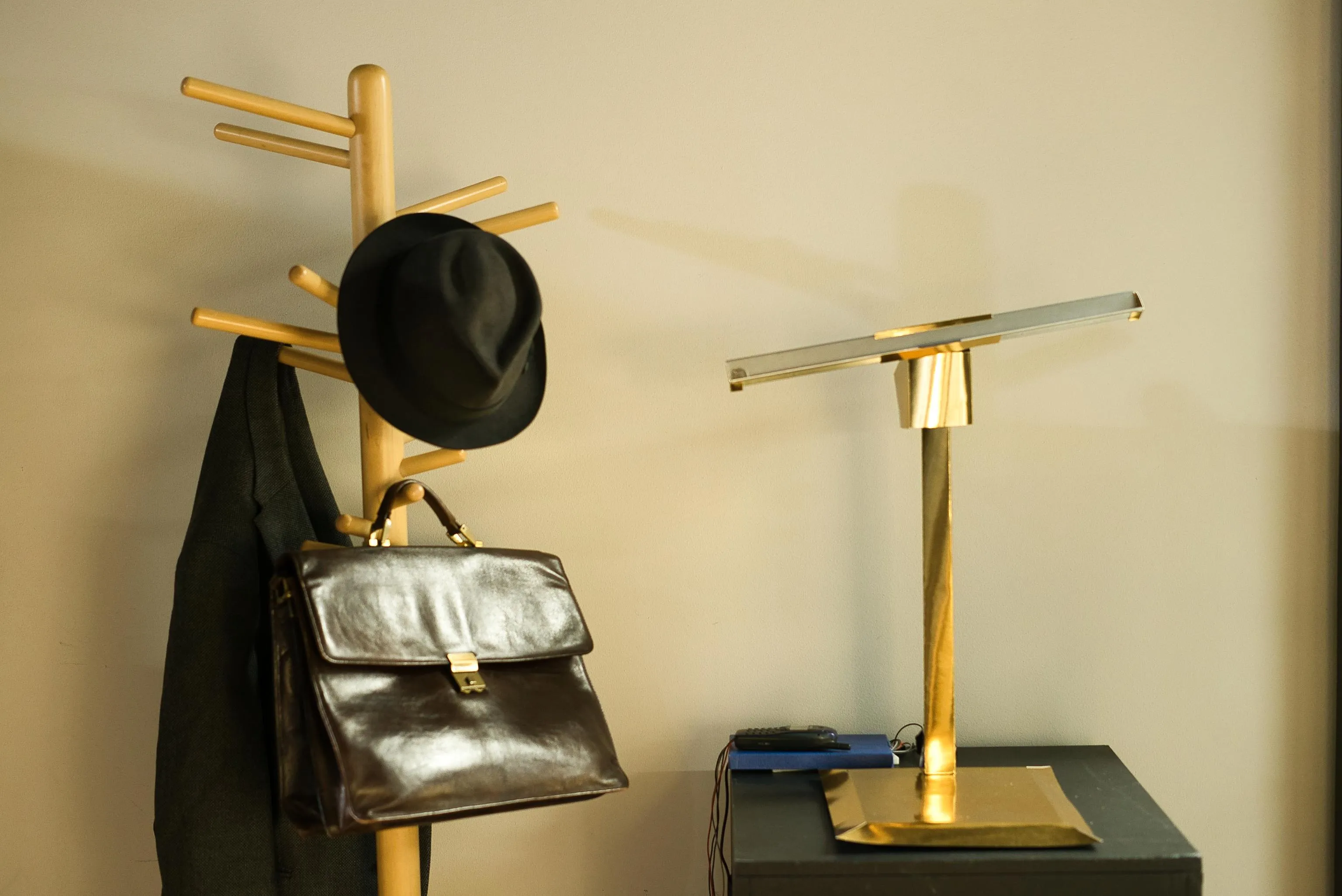 A jacket, hat and suitcase next to a golden pedestal.