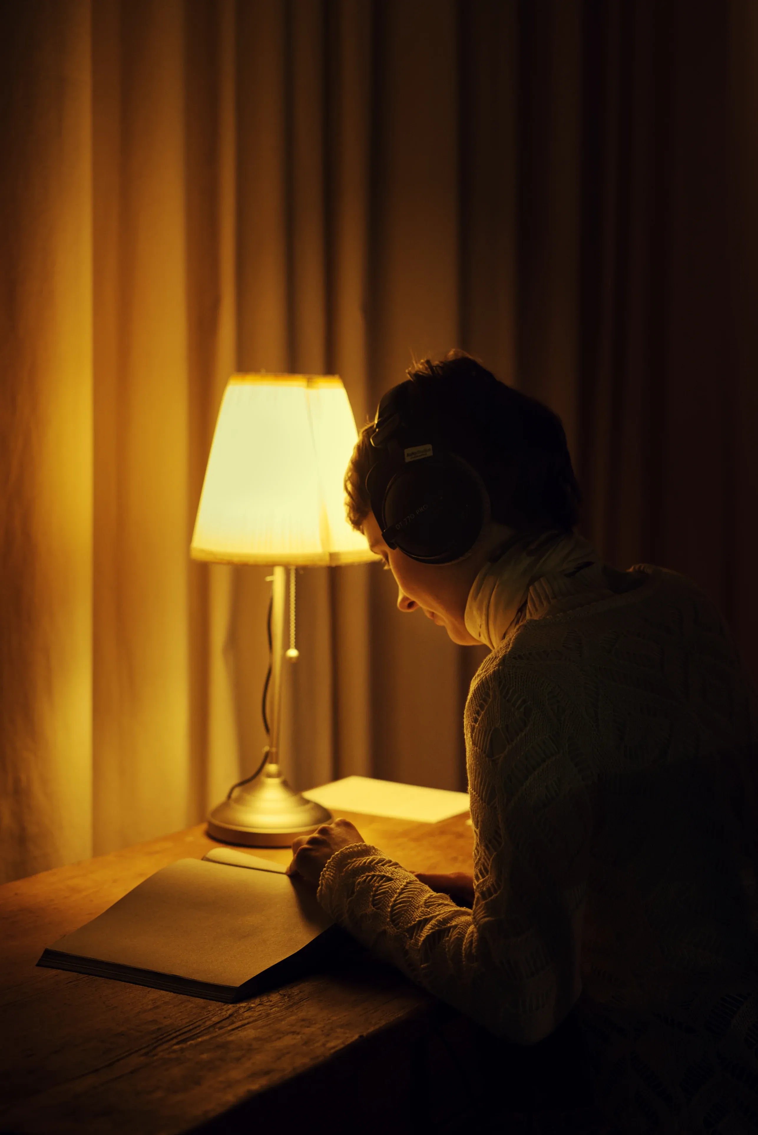 A person wearing headphones reading a book on a warmly lit wooden table.